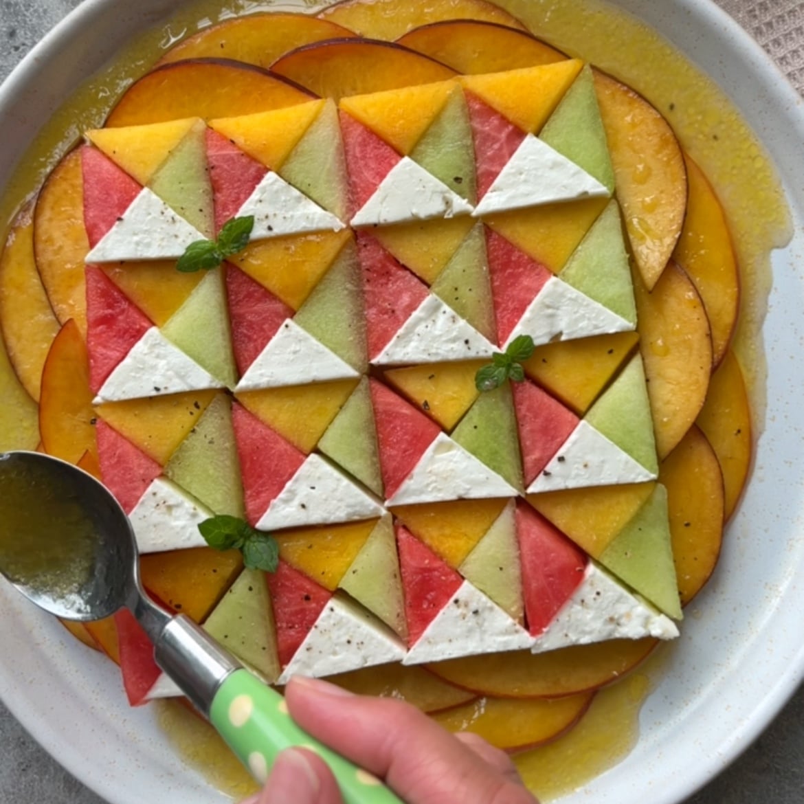 A hands spoons yellow vinaigrette onto a colorful salad with a beautiful geometric pattern.