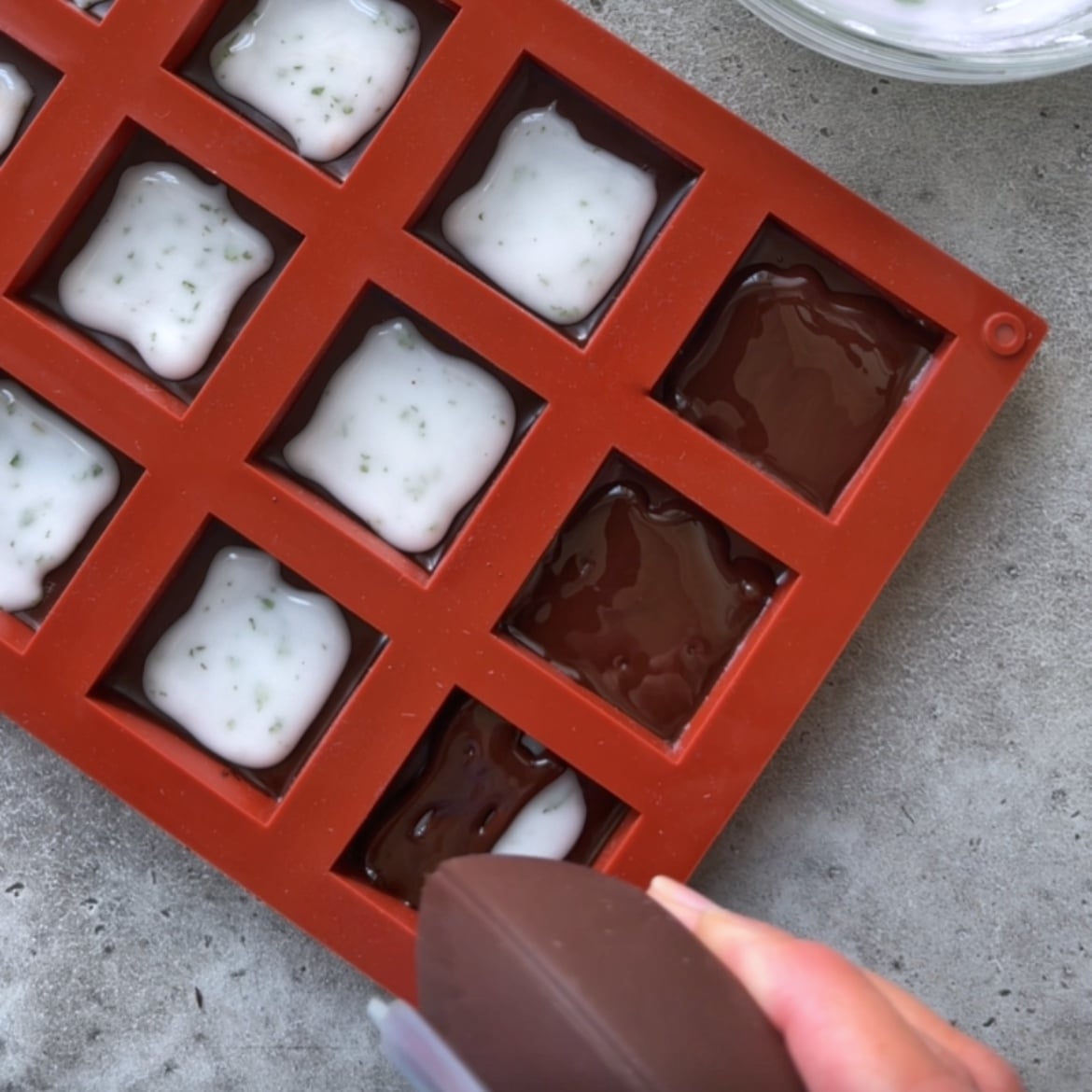 A piping utensil fills melted chocolate on top of mint filling in a red silicone mold.