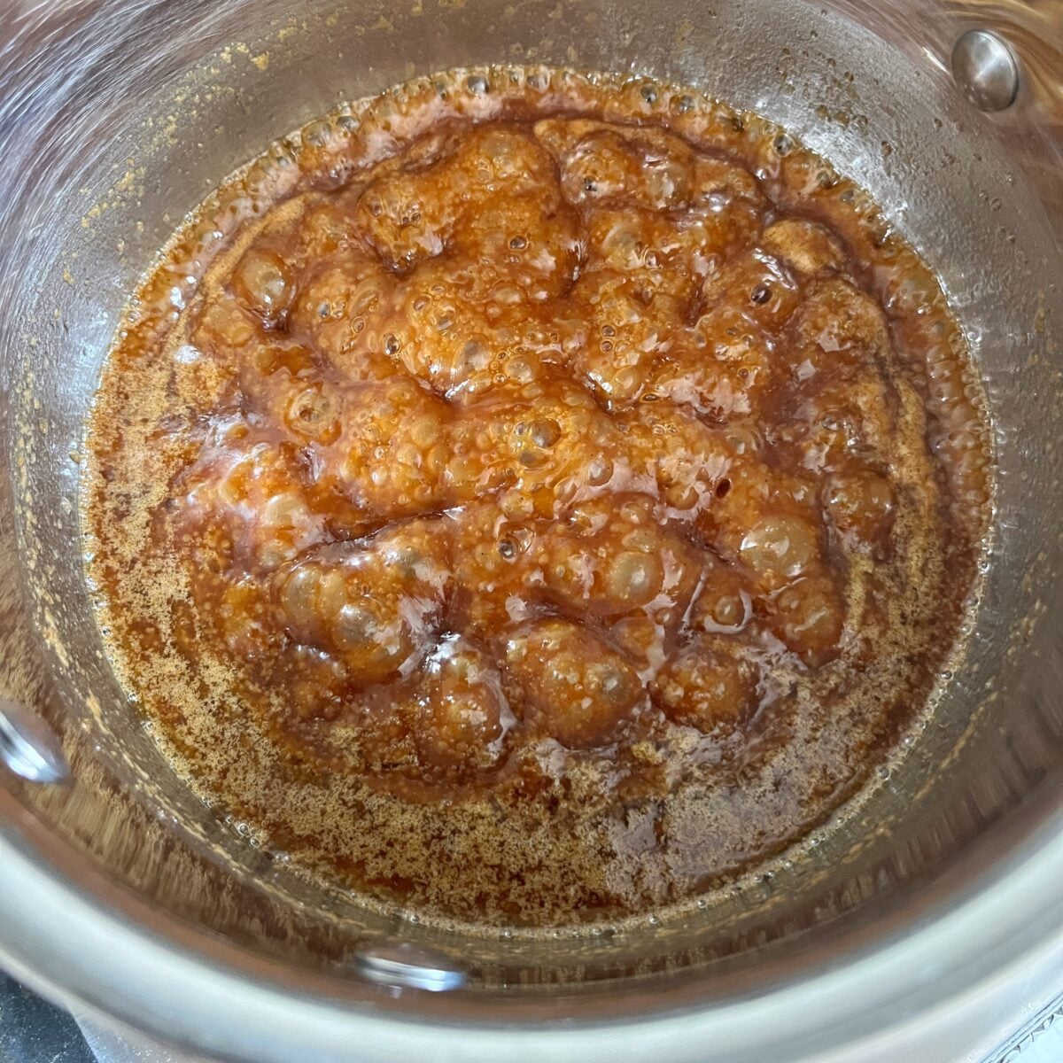A saucepan filled with bubbling caramel as it cooks, showing a golden-brown color.