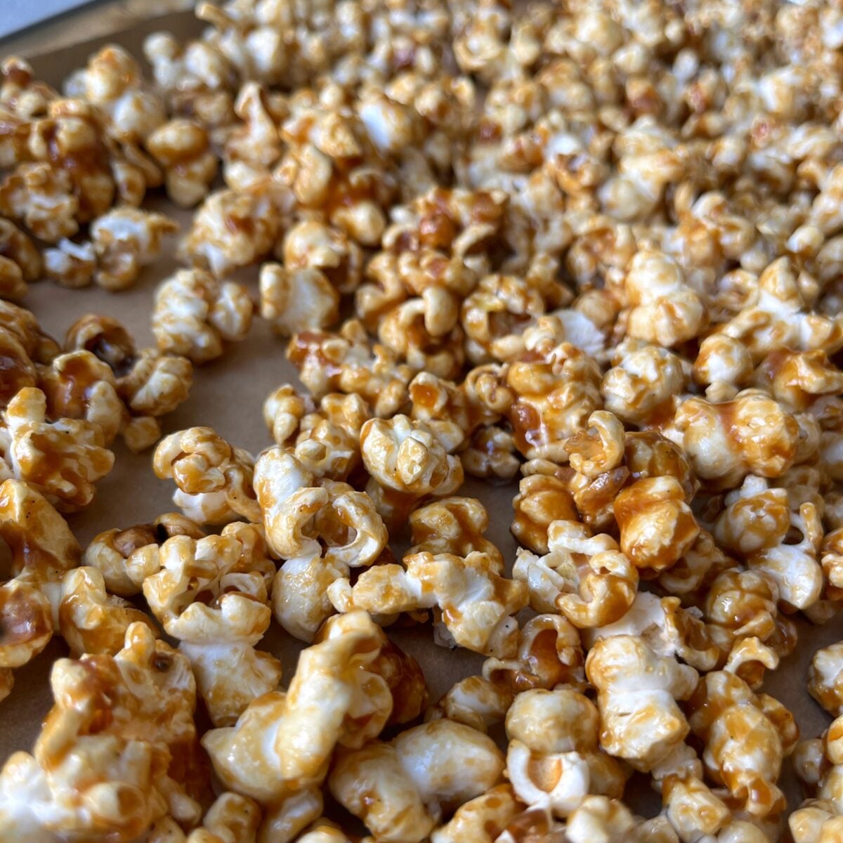 Close-up of Homemade Caramel Popcorn, each piece coated in rich caramel and spread out on a lined baking sheet.