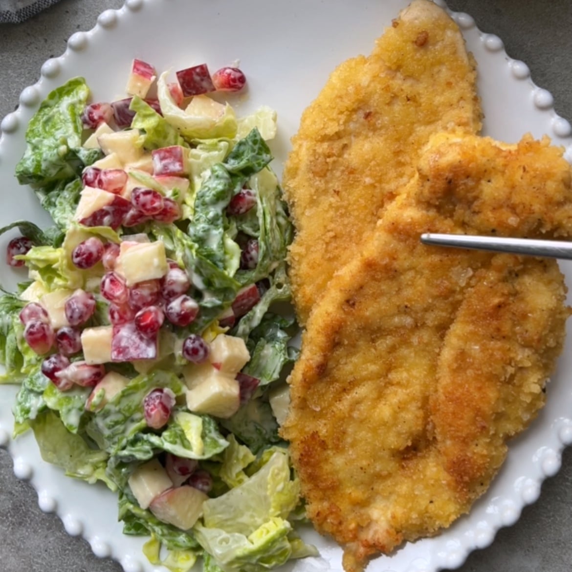 Two pieces of Milanese Chicken cutlets on a plate next to a green salad with diced apples in a creamy dressing.