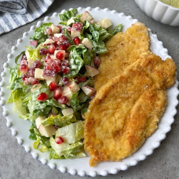 A plate with two breaded chicken cutlets and a green salad with pomegranate seeds and diced apples.