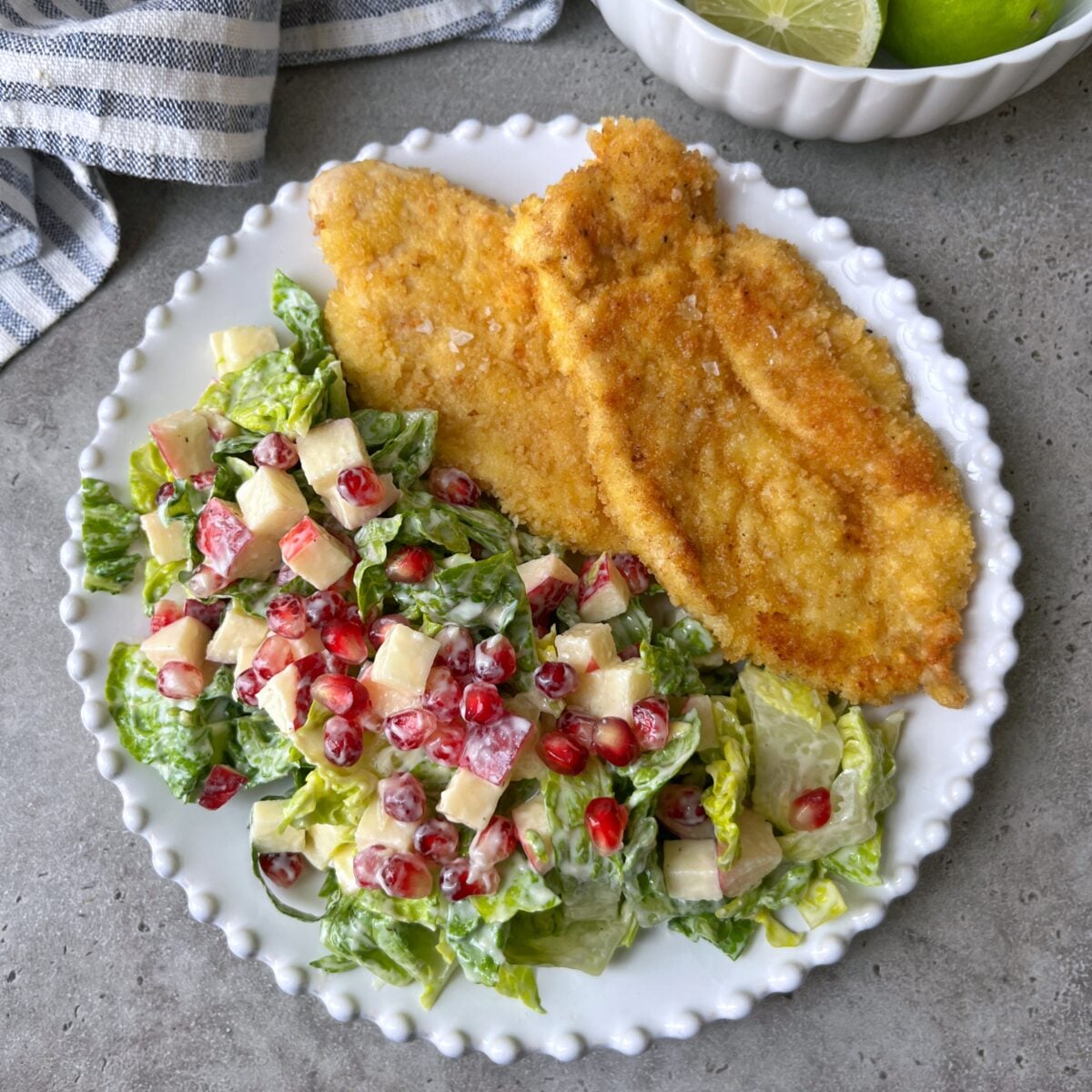 Two breaded, fried chicken cutlets alongside a green salad tossed with chopped apples and pomegranate seeds.