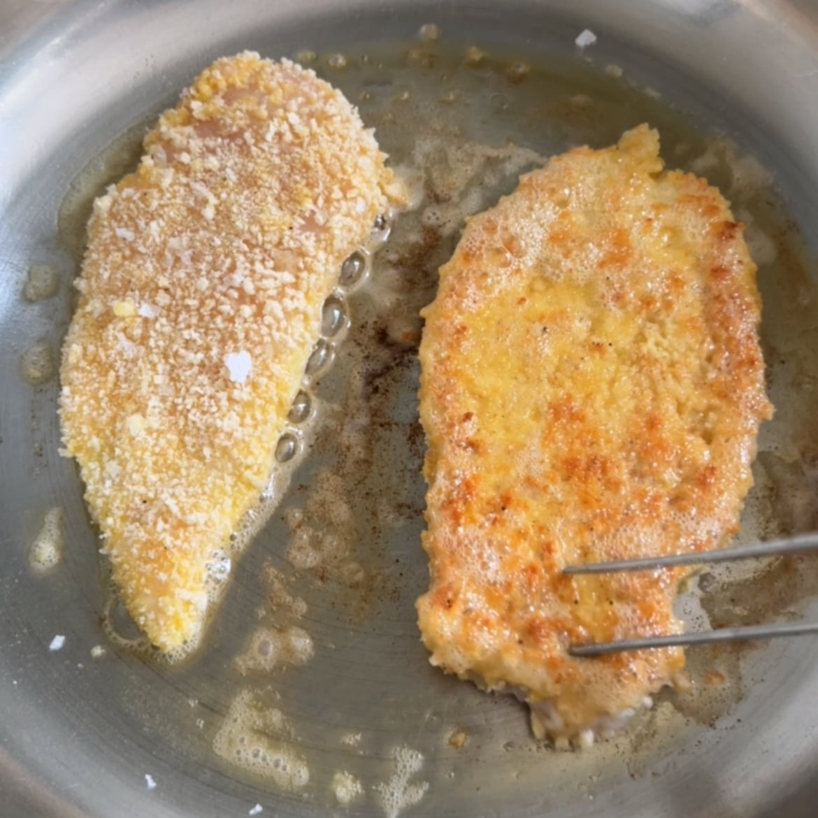 Two Milanese Chicken cutlets are frying in a pan.