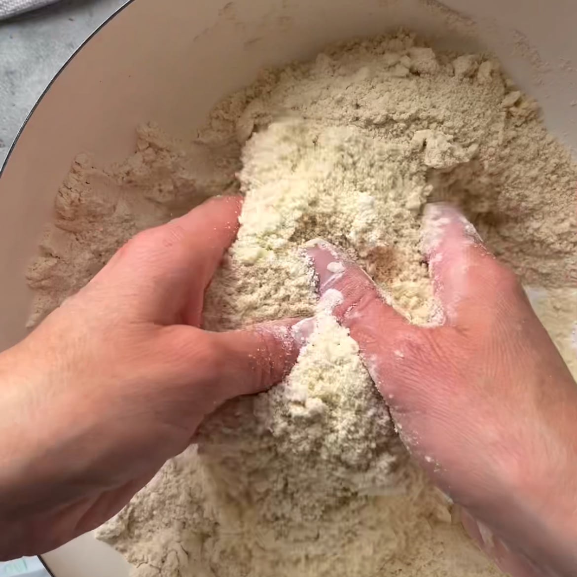 Two hands rub cold butter into a flour mixture.