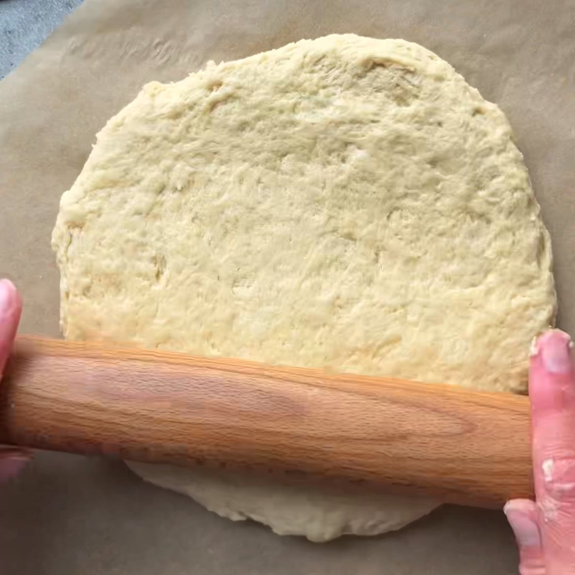 Two hands are rolling out dough with a wooden rolling pin.