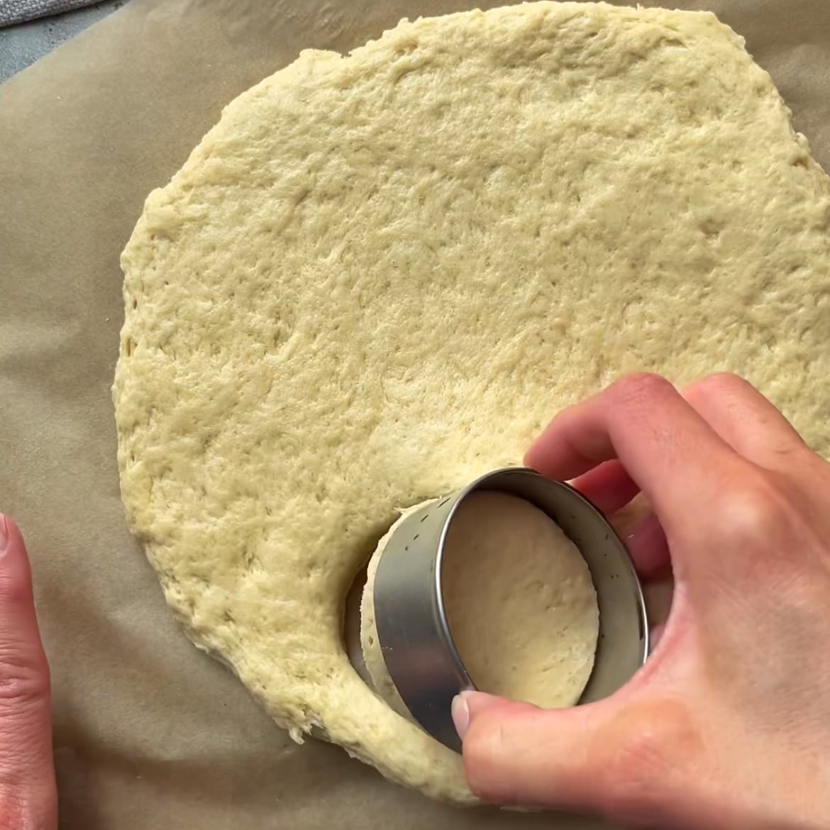 A hand is cutting out scones from a rolled out dough with a round cutter.