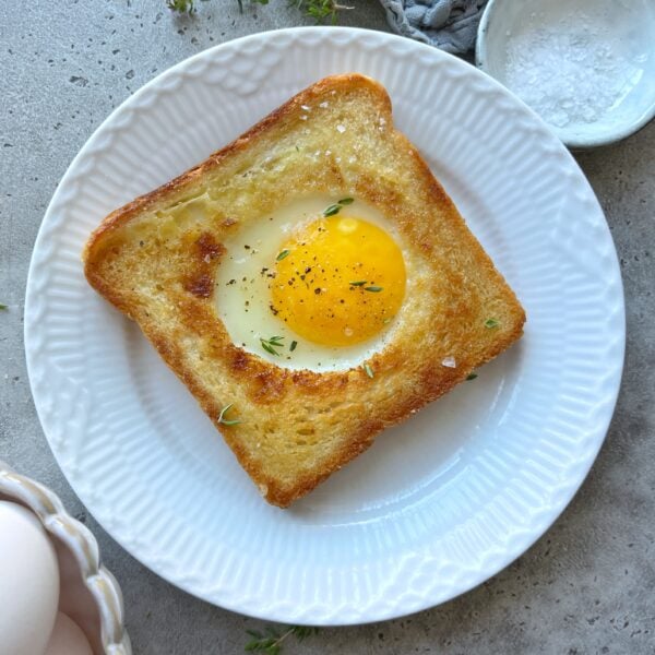 Toasted white bread filled with an egg in the center and topped with fresh thyme.