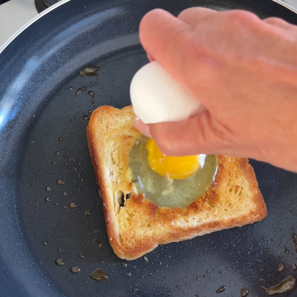A hand cracks open an egg into a hole cut out from a piece of toast.