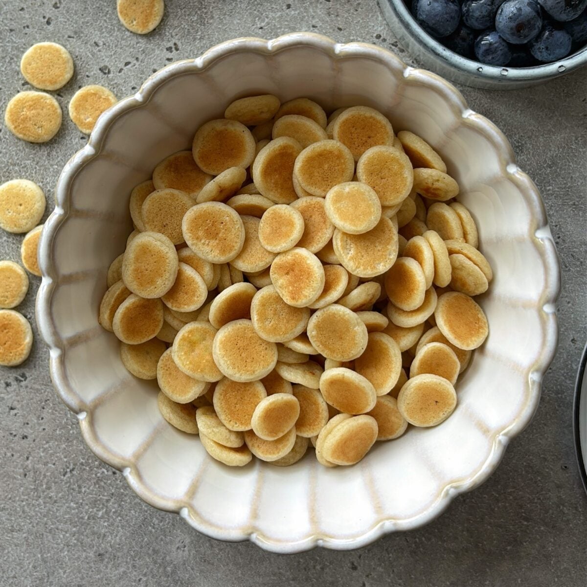 A bowl of mini pancakes ready to be topped with milk, maple syrup, and blueberries.