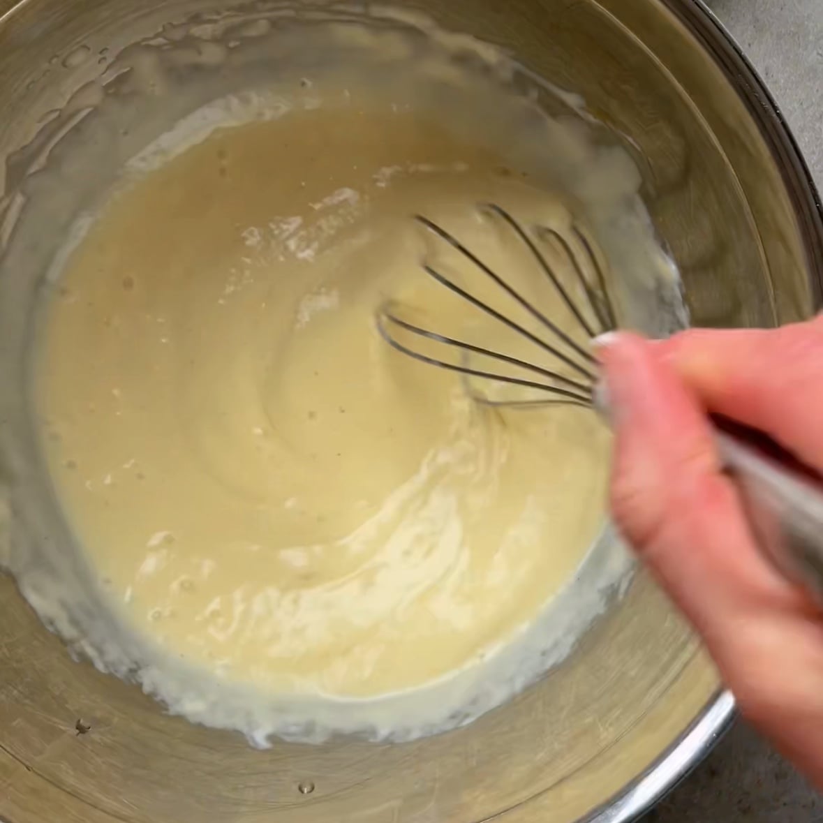 A whisk mixing pancake batter in a stainless steel bowl.