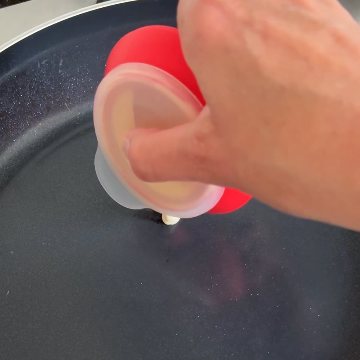 A piping utensil dots pancake batter onto a warm skillet.