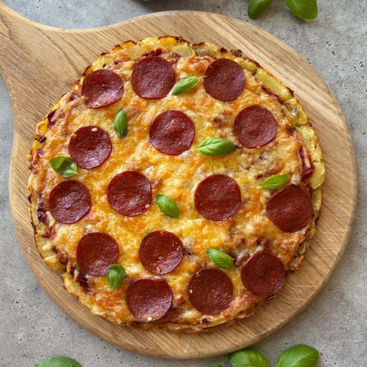 Smashed potato pizza topped with basil on a chopping board.