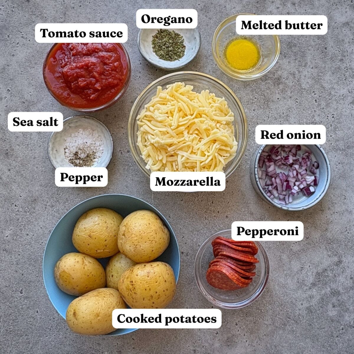 Ingredients for Smashed Potato Pizza featuring bowls of cooked potatoes, tomato sauce, melted butter, mozzarella, diced red onion, pepperoni, oregano, and sea salt and pepper.