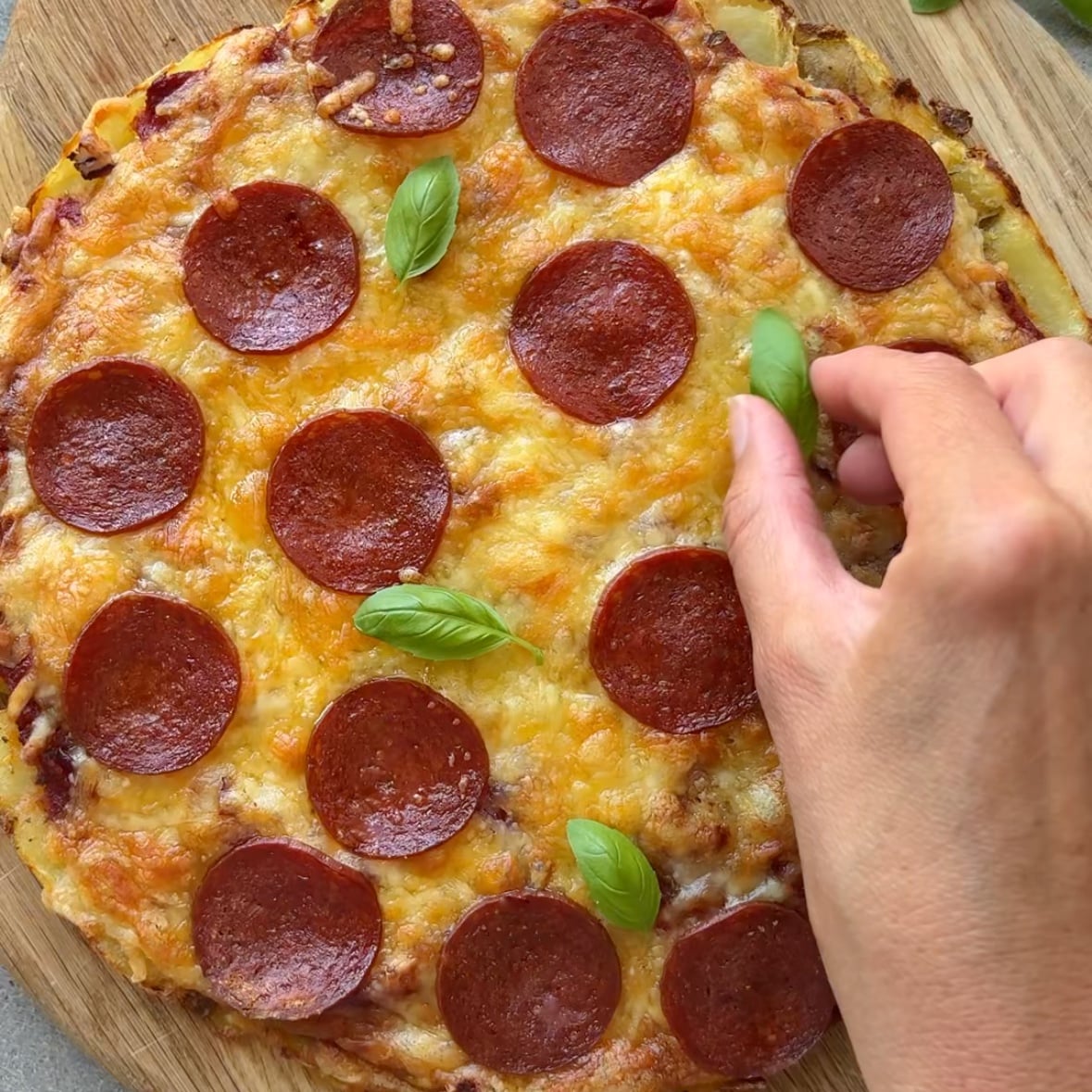 A hand places fresh basil onto a smashed potato pizza.