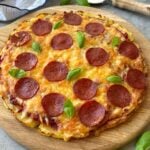 Side view of a smashed potato pizza with pepperoni and fresh basil.
