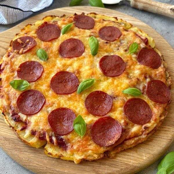 Side view of a smashed potato pizza with pepperoni and fresh basil.