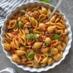 A bowl of freshly made Spicy Italian Sausage Pasta with a striped tea towel and fresh basil in the background.