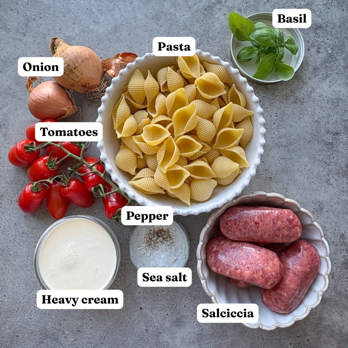 Ingredients for Spicy Italian Sausage Pasta featuring bowls of pasta, Italian sausages, onion, heavy cream, tomatoes, fresh basil, sea salt, and pepper.
