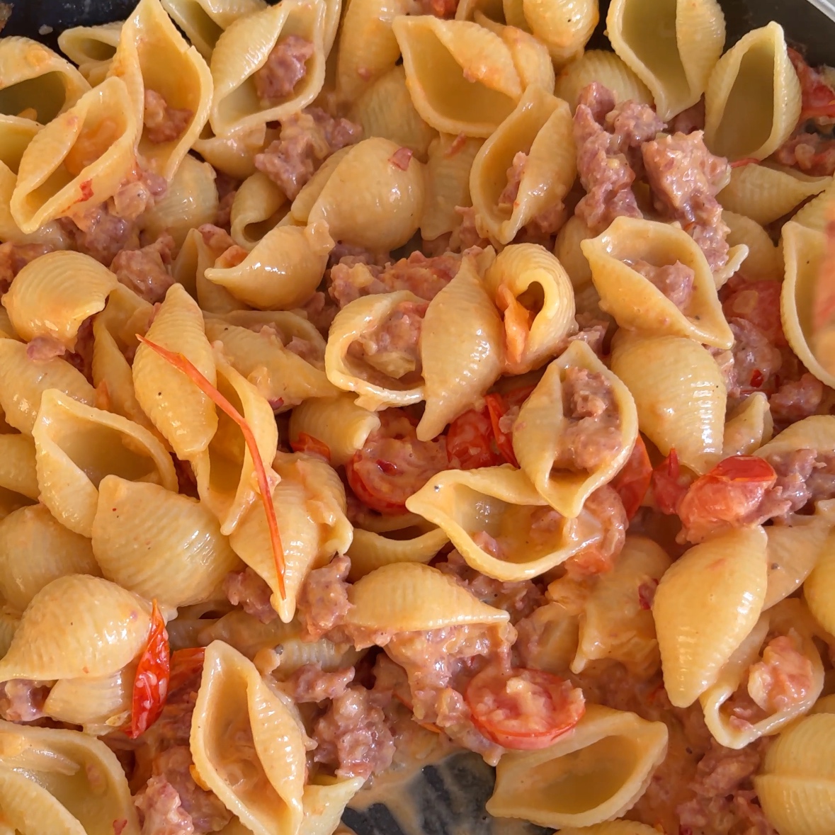 A closeup of pasta being added to the spicy Italian sausage sauce.