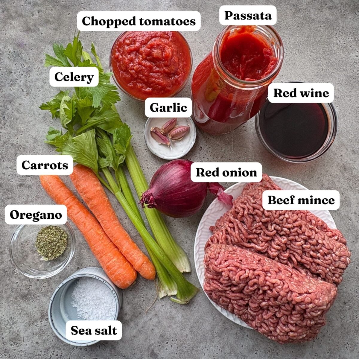 Ingredients for Beef Bolognese featuring a jar of passata, 3 celery stalks, 2 carrots, a plate of beef mince, red wine, 1 red onion, 3 cloves of garlic, sea salt, and oregano.