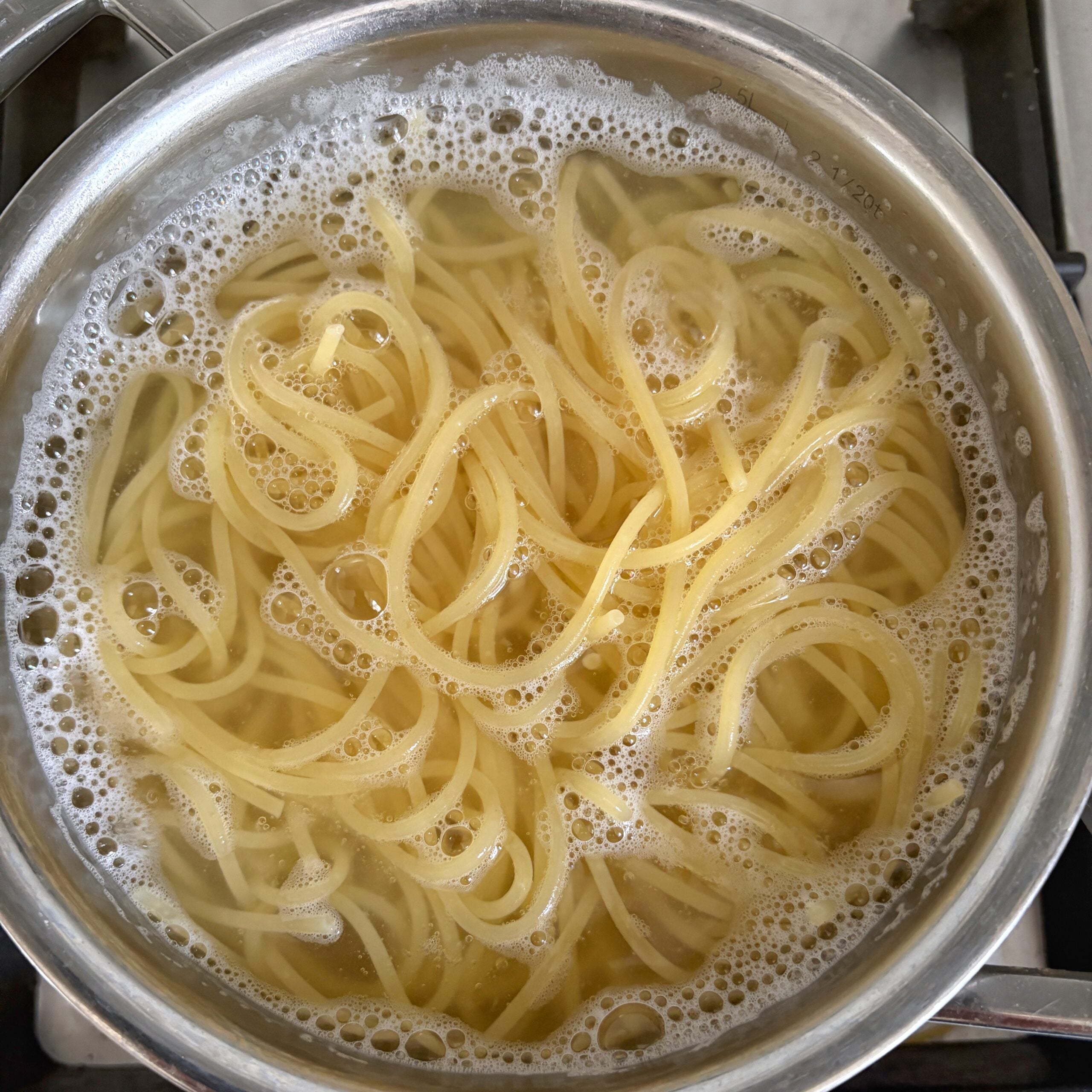 Spaghetti cooking in a medium pot.