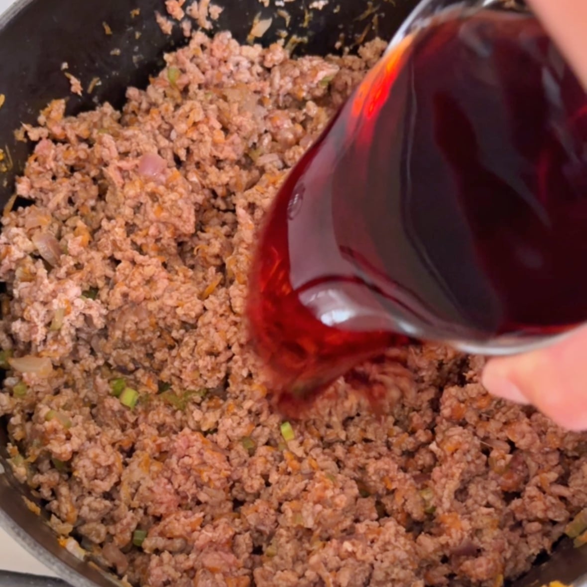 Adding red wine to the beef bolognese.