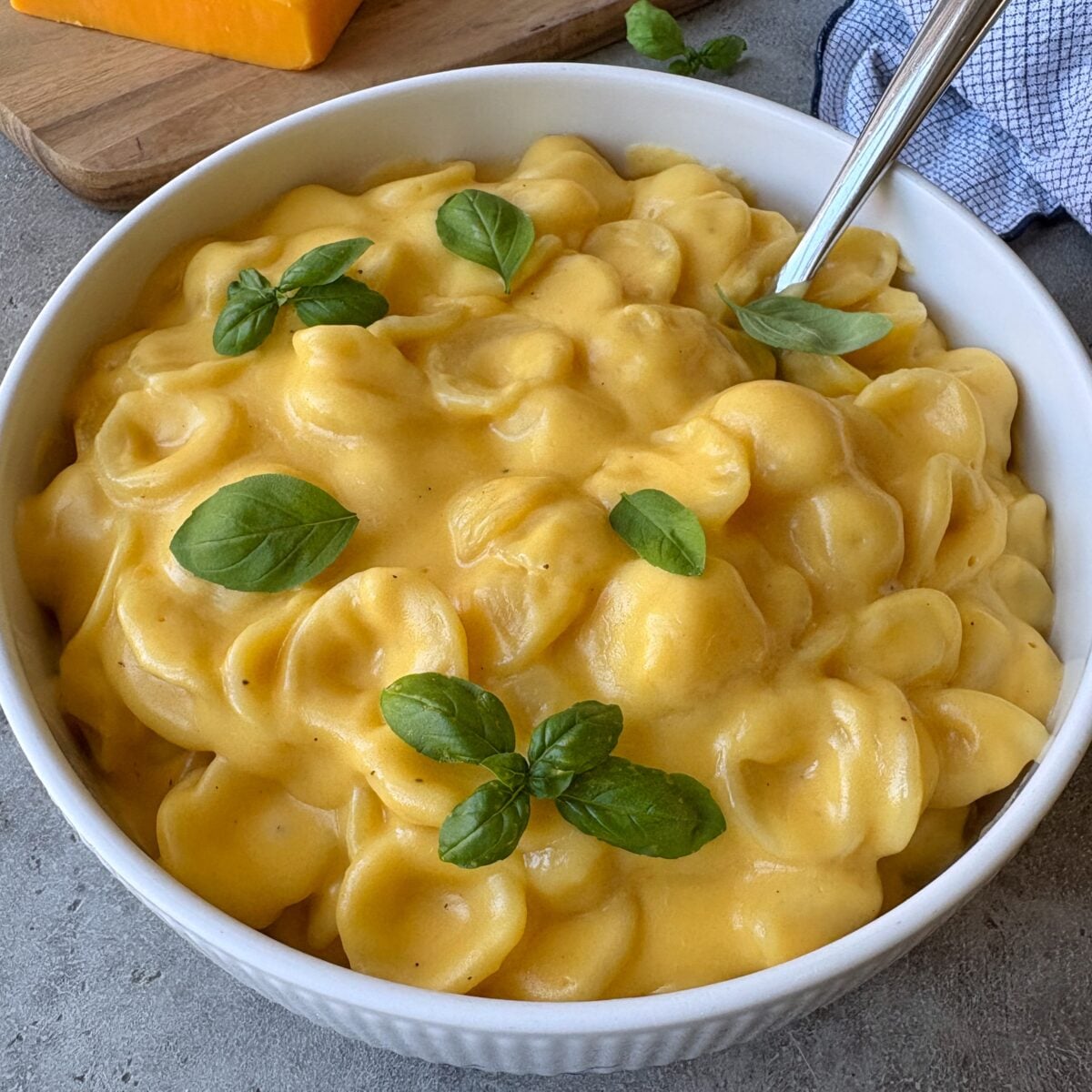 A large bowl of red cheddar Mac and cheese topped with fresh basil.