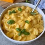 A large bowl of red cheddar Mac and cheese topped with fresh basil.