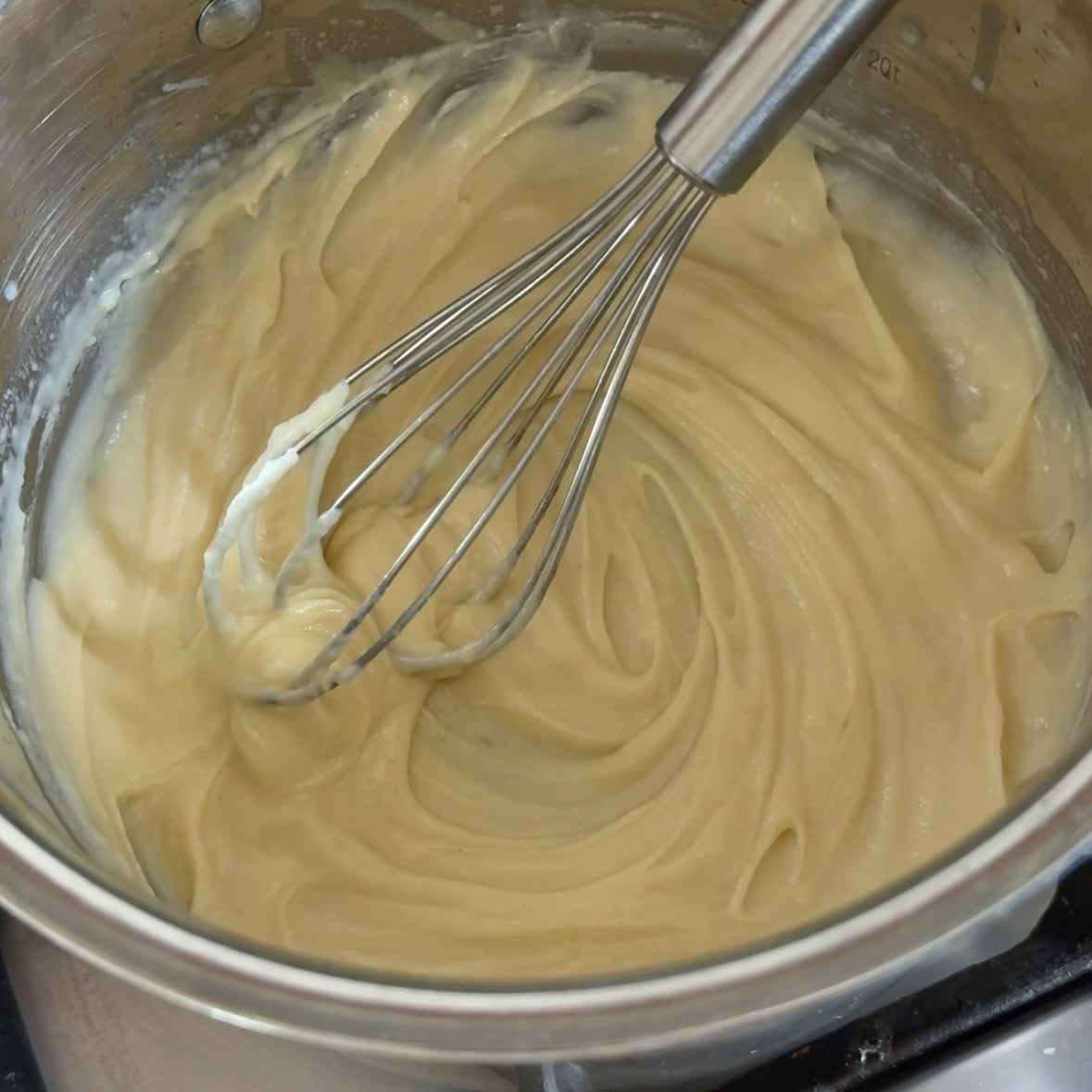 A hand is whisking milk into a white sauce in a saucepan.