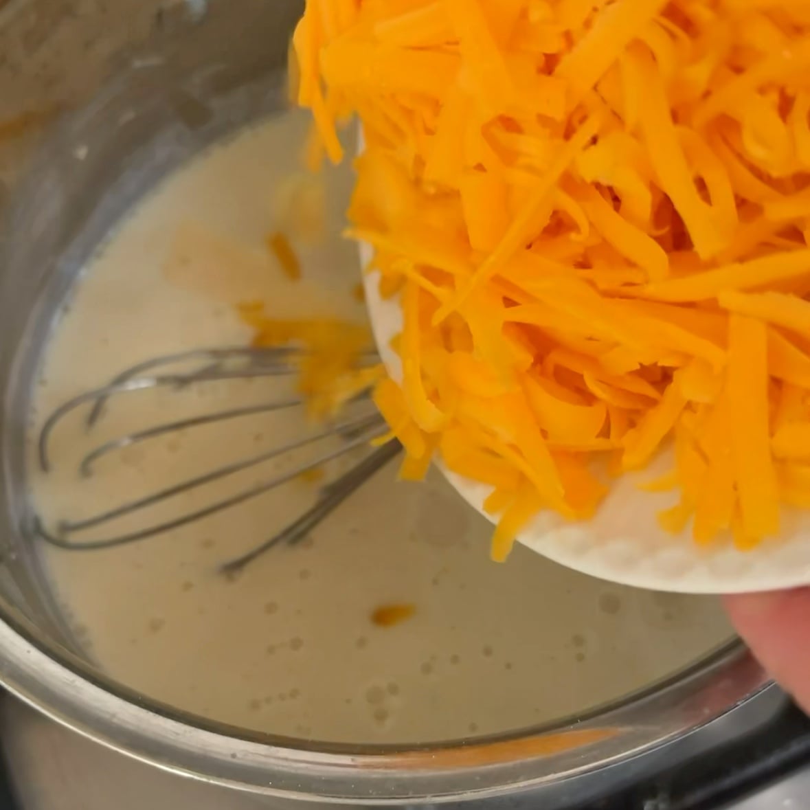 Red cheddar is being added to a white sauce.