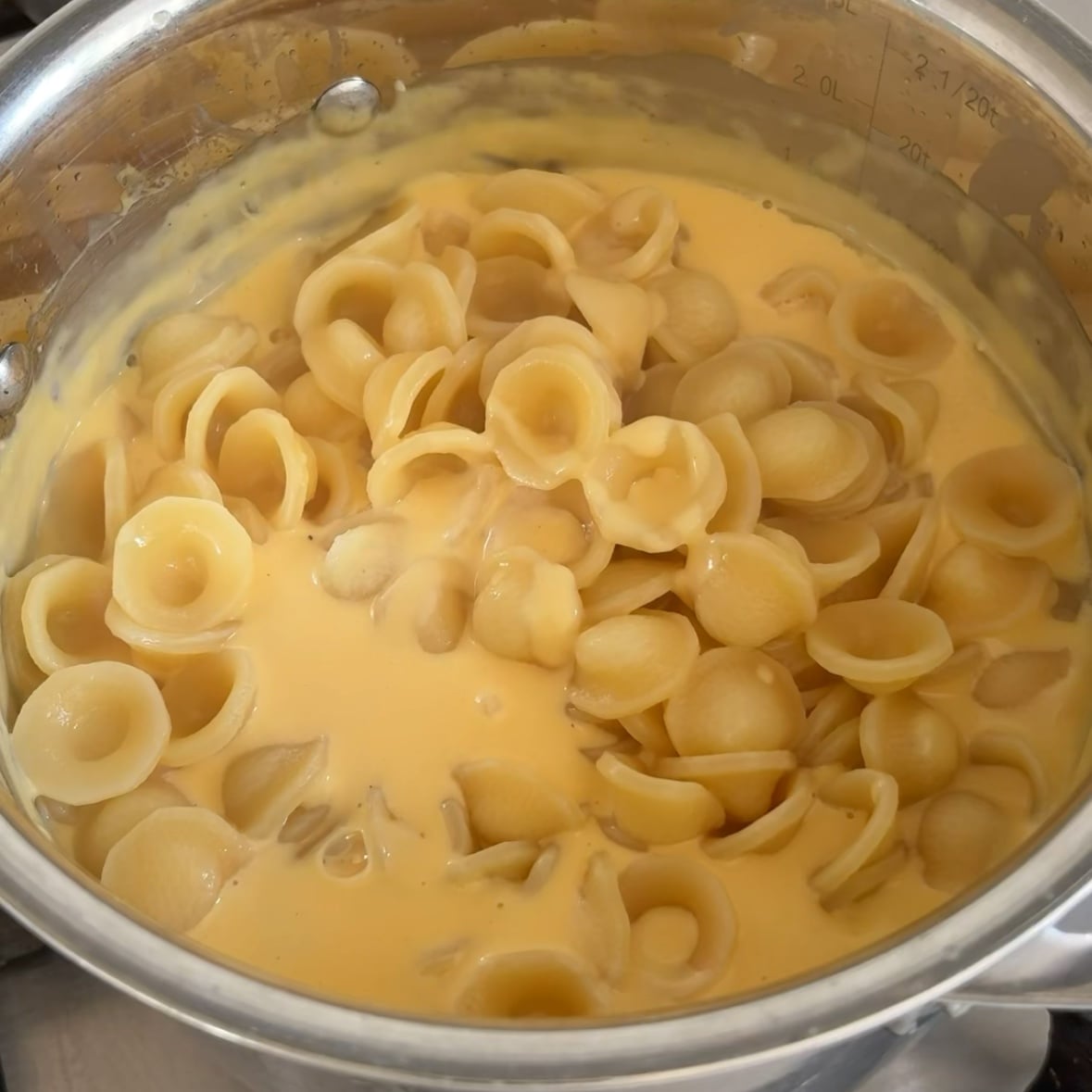 Pasta is being poured into a saucepan with red cheesy sauce.