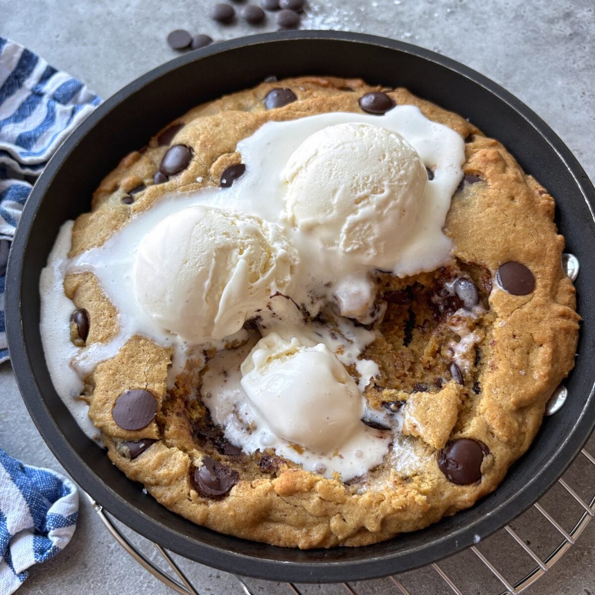 A close up of a chocolate chip pizookie topped with vanilla ice cream with the center scooped out.