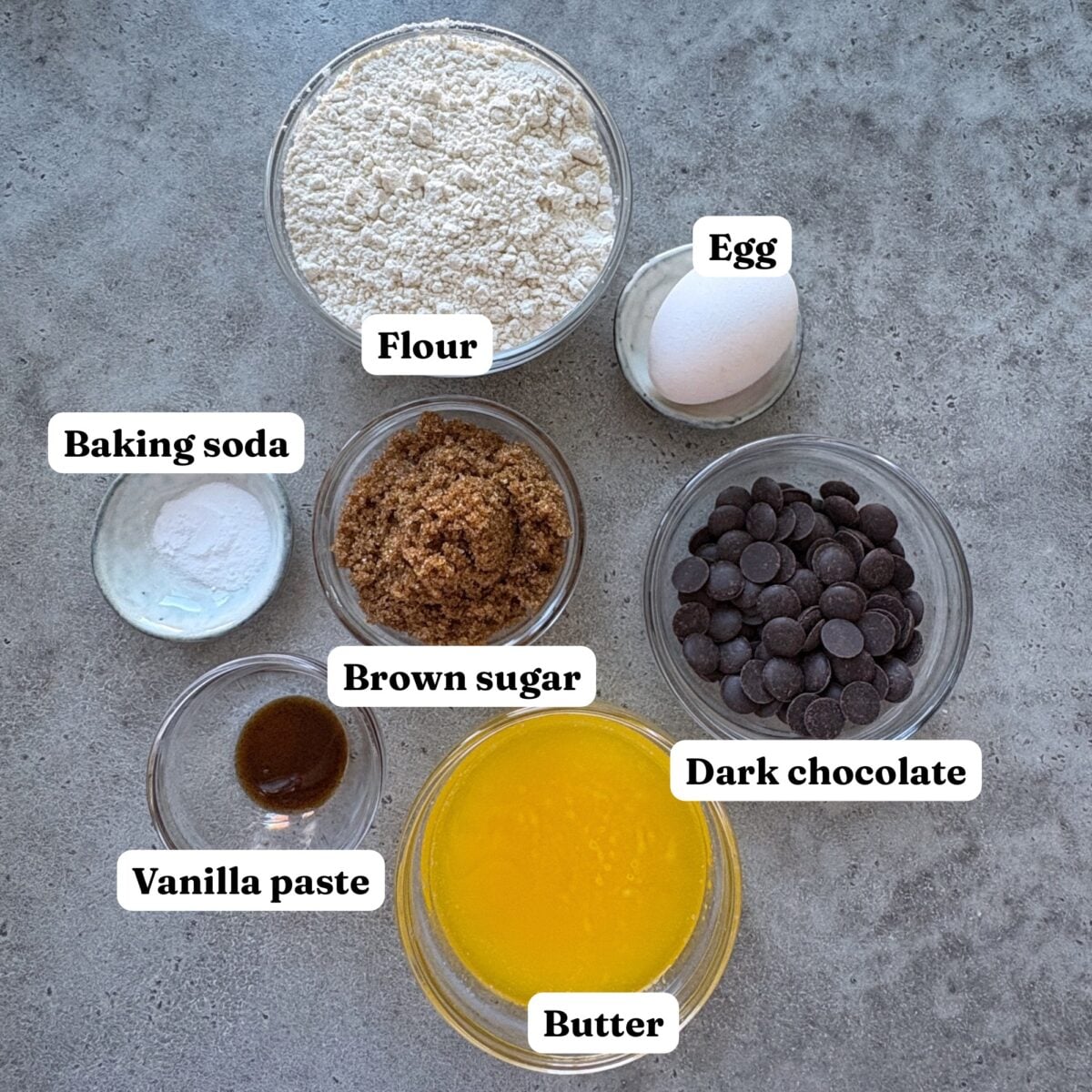 Ingredients for Chocolate Chip Pizookie. Features bowls of melted butter, flour, vanilla paste, chocolate chips, baking soda, brown sugar, and an egg.