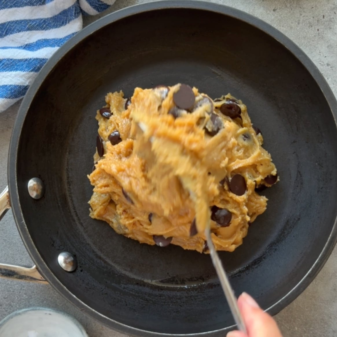 Chocolate chip cookie dough is being spooned into a prepared skillet.