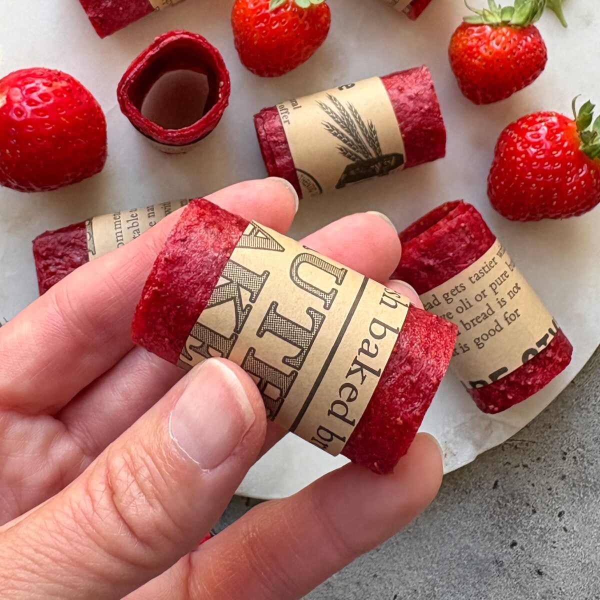 A close up of a strawberry fruit roll up with more roll ups in the background arranged on a white marble plate.