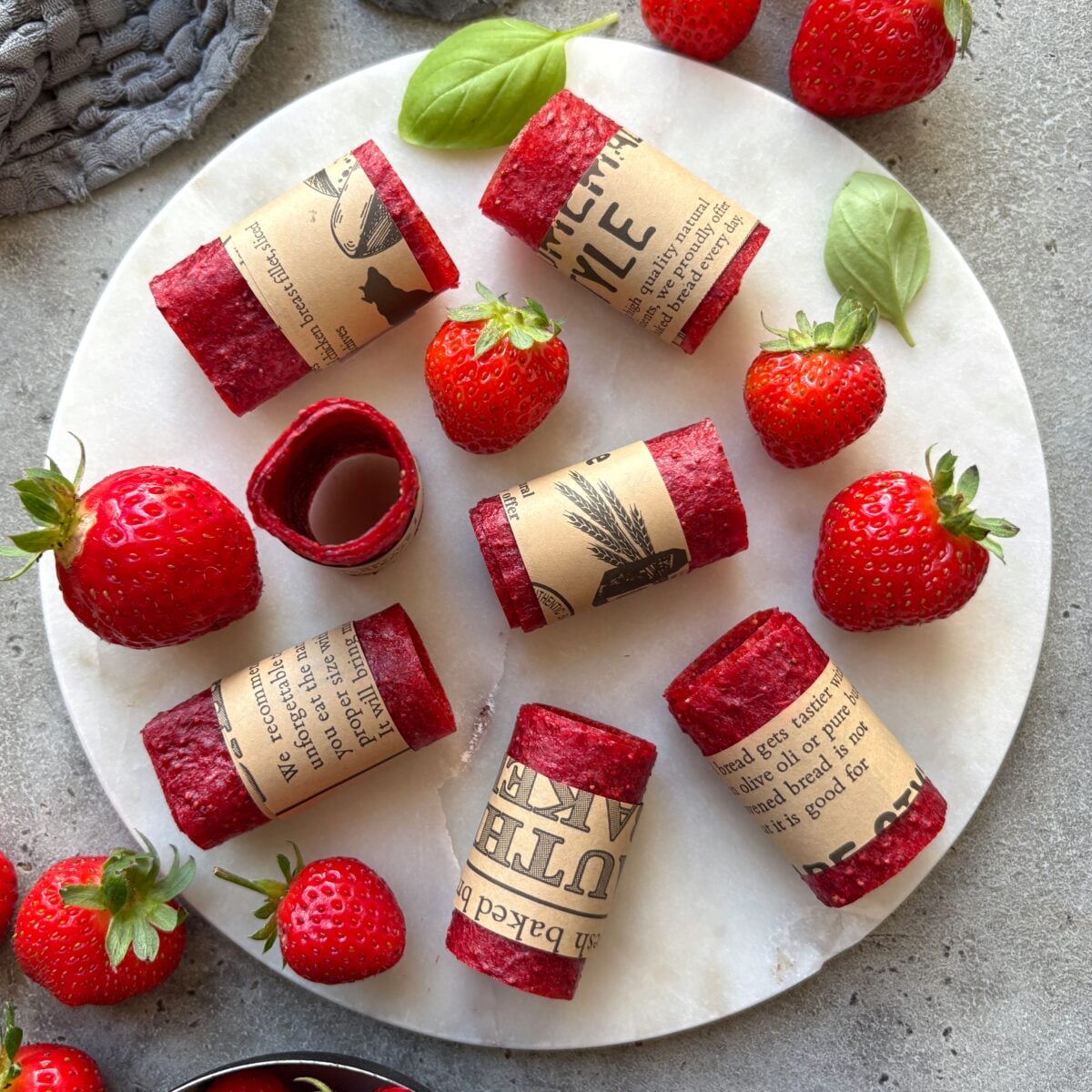 Seven strawberry fruit leather roll ups arranged on a white marble plate.