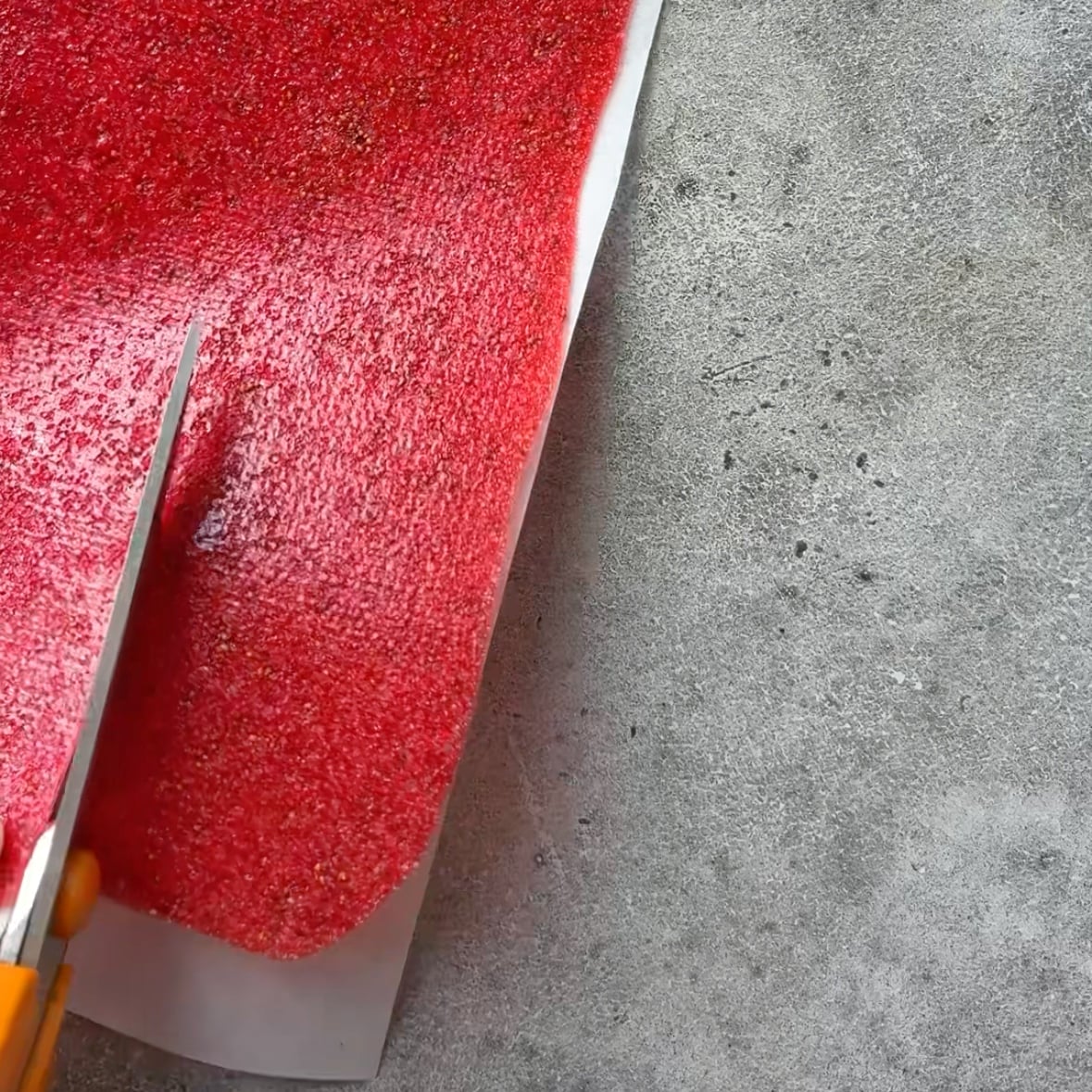 Scissors cut strips of strawberry fruit leather.