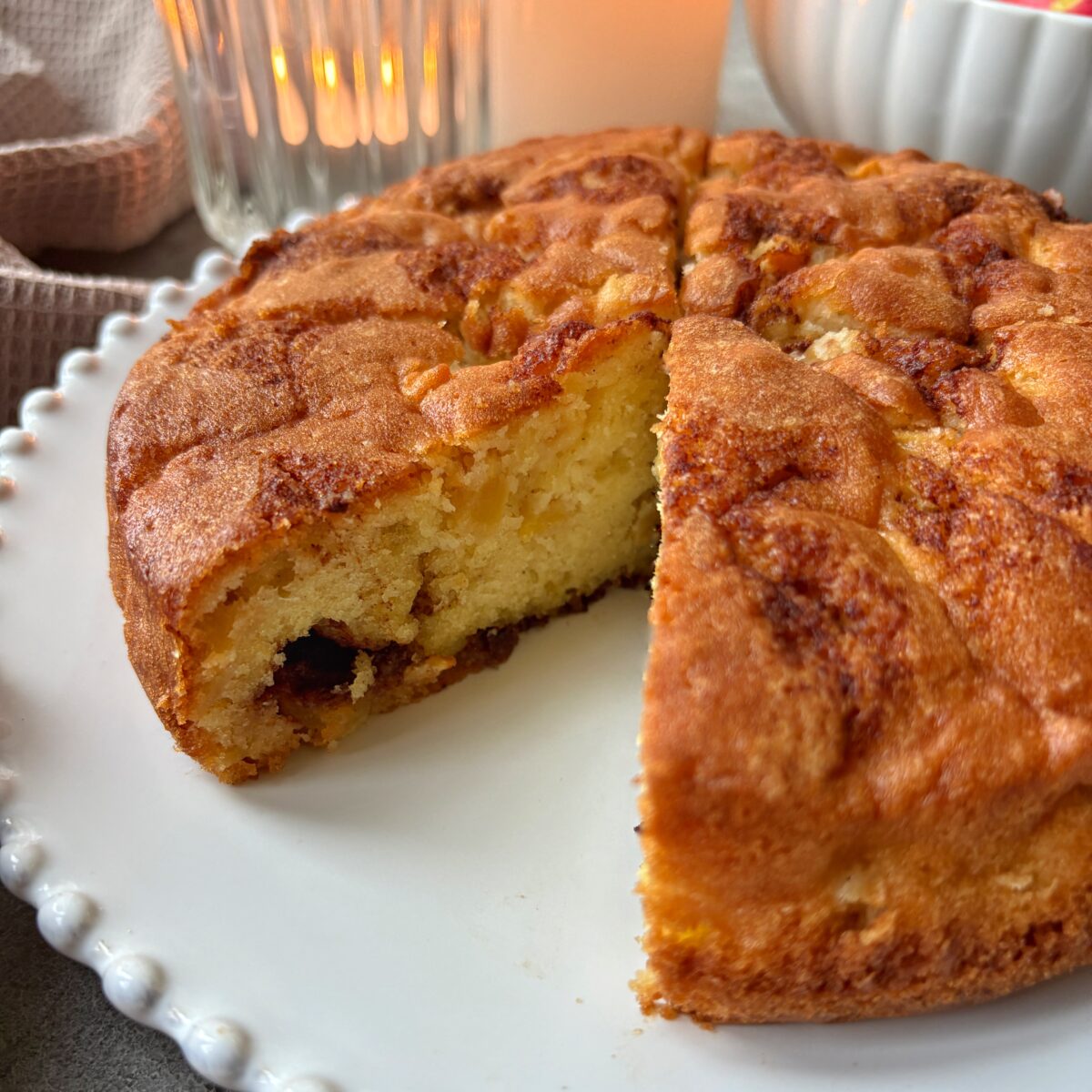 A golden-brown Cinnamon Apple Cake with a piece cut out of it.