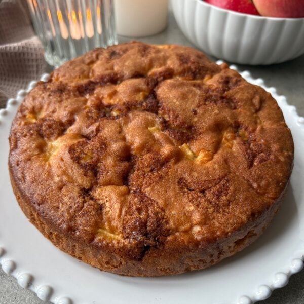 A golden-baked Cinnamon Apple Cake on a white platter.