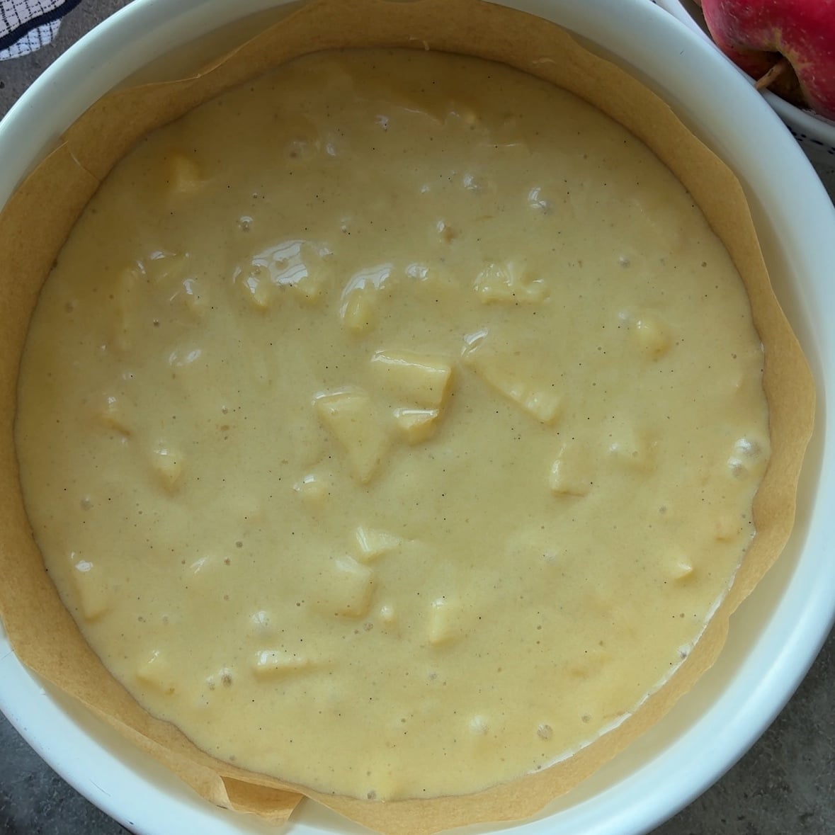 Unbaked Cinnamon Apple Cake batter with visible apple chunks in a round baking pan lined with parchment paper.