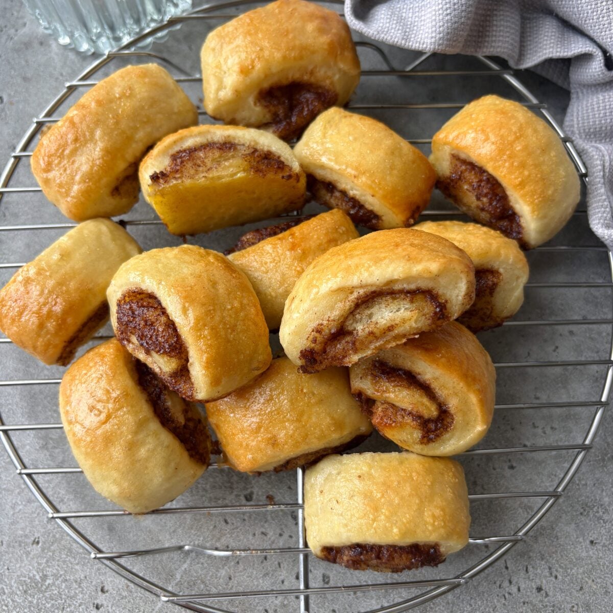 Golden brown mini cinnamon rolls cooling on a round metal rack, with a grey cloth in the background.
