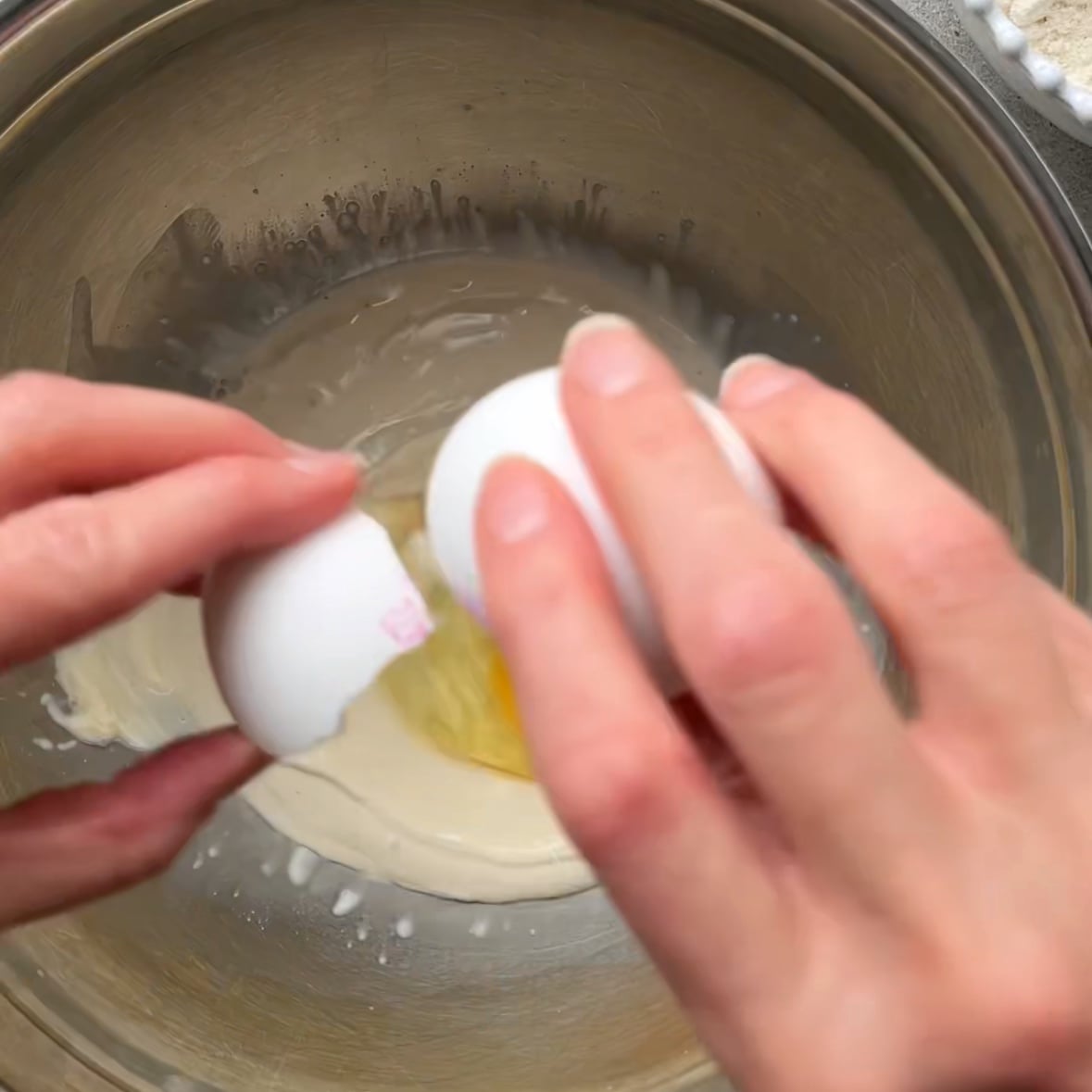 A person cracks an egg into a stainless steel bowl to make a mini cinnamon roll dough.