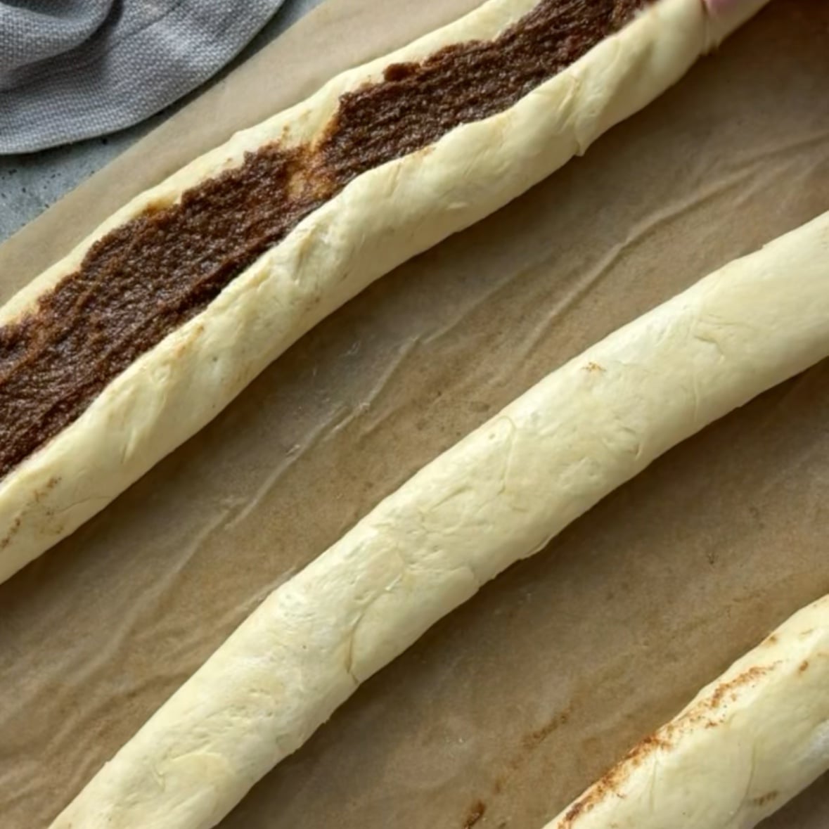 Three sections of cinnamon roll dough filled with brown sugar, butter, and cinnamon, are ready to be cut into rolls.