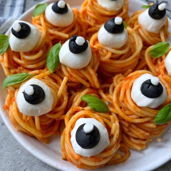 A plate of spaghetti nests topped with mozzarella balls, black olive slices, and basil leaves, arranged to look like eyeballs.