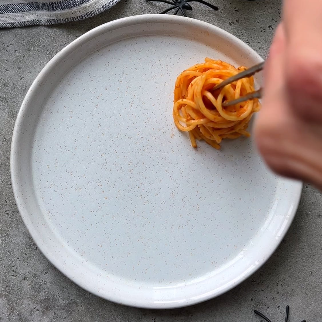 A hand uses food tweezers to arrange a tomato and spaghetti nest onto a serving platter.